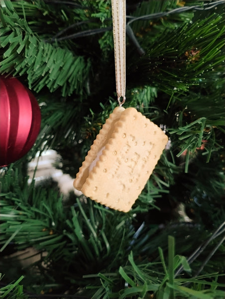 Decorative biscuit ornament hanging on a Christmas tree with a red ball in the background.