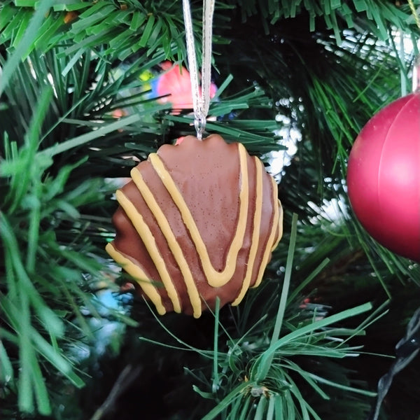 Decorative cookie ornament hanging on a Christmas tree with green branches and pink ball ornament.