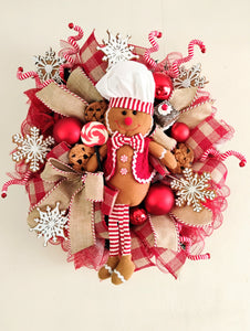 Decorative wreath with gingerbread man, candy, and festive ribbons on a beige background