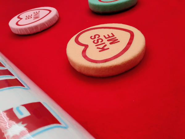 Heart-shaped candy with 'Kiss Me' text on a red background