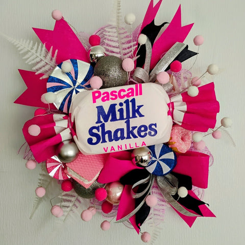 Non-traditional Christmas wreath with a large Pascall Milk Shakes lolly, surrounded by colorful picks and sprays. 