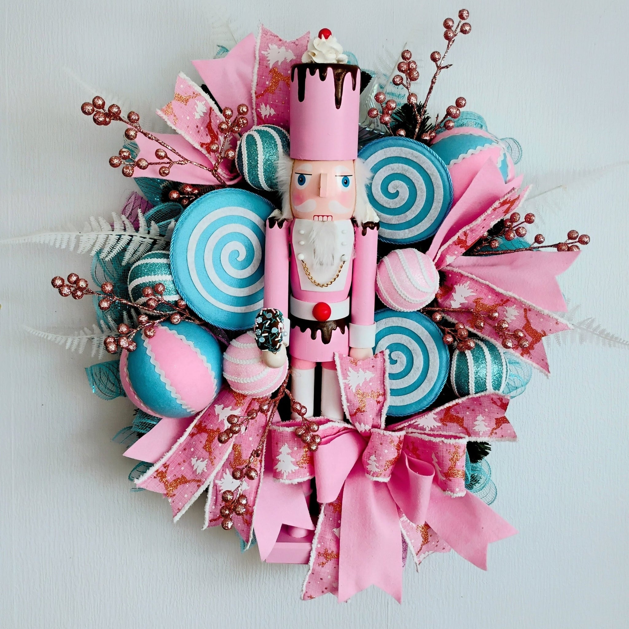 Decorative wreath with a nutcracker, candy-themed decorations, and pink ribbons on a white background