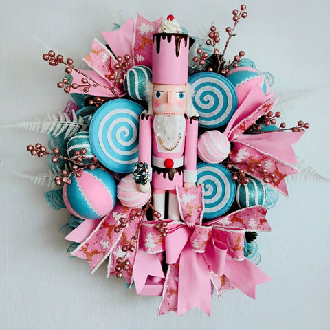 Decorative wreath with a nutcracker, candy-themed decorations, and pink ribbons on a white background