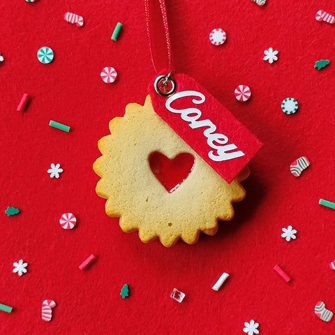 Decorative cookie with a heart cutout and 'Corey' tag on a red background with colorful sprinkles.