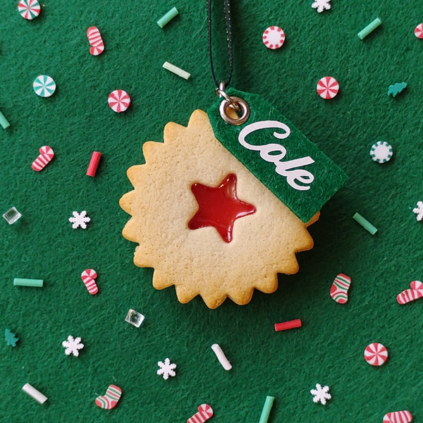 Decorative cookie with a red star and 'COLE' tag on a green background with festive sprinkles.