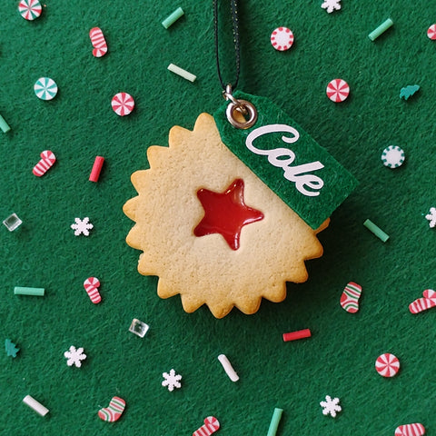 Decorative cookie with a red star and 'COLE' tag on a green background with festive sprinkles.
