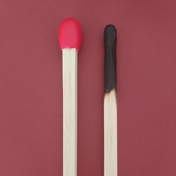 Two matches, one with a red head and the other with a black burnt head on a burgundy background. 