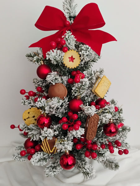 Small Decorative Christmas tree with biscuit ornaments, red baubles and berries, and a large red bow on a white background